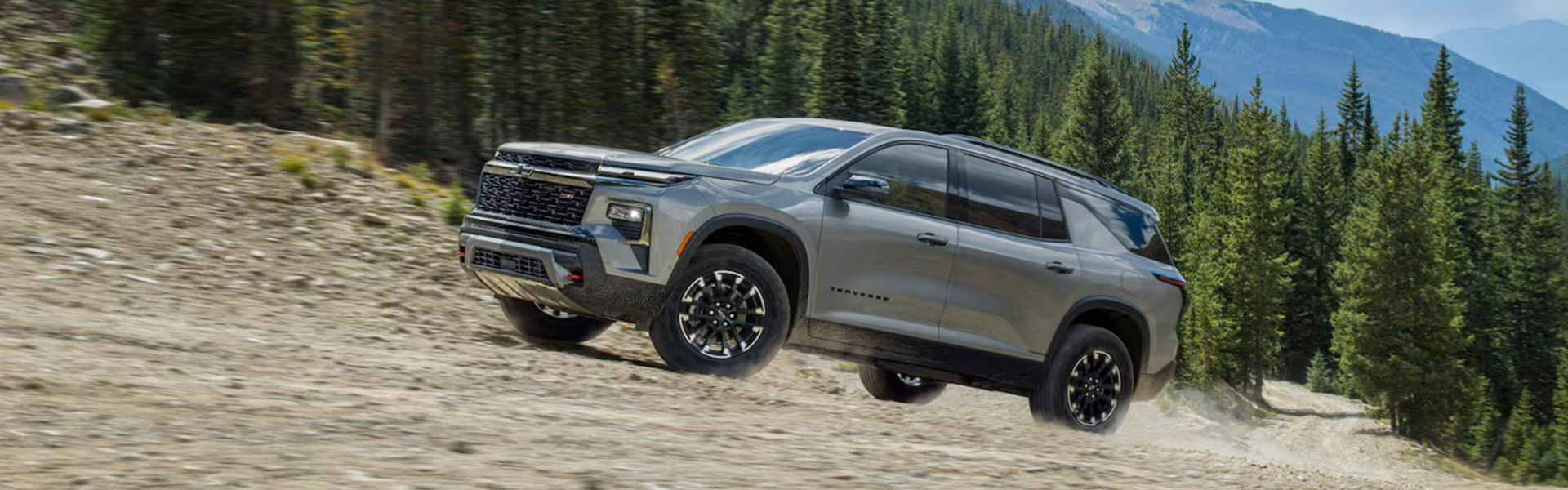 2024 Chevrolet Traverse in grey running with trees and mountain background BANNER