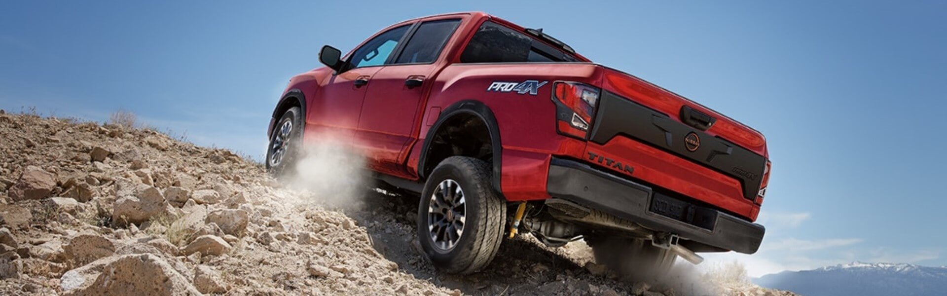 2024 Nissan TITAN In Red Driving Up A Large Rock Pile Banner