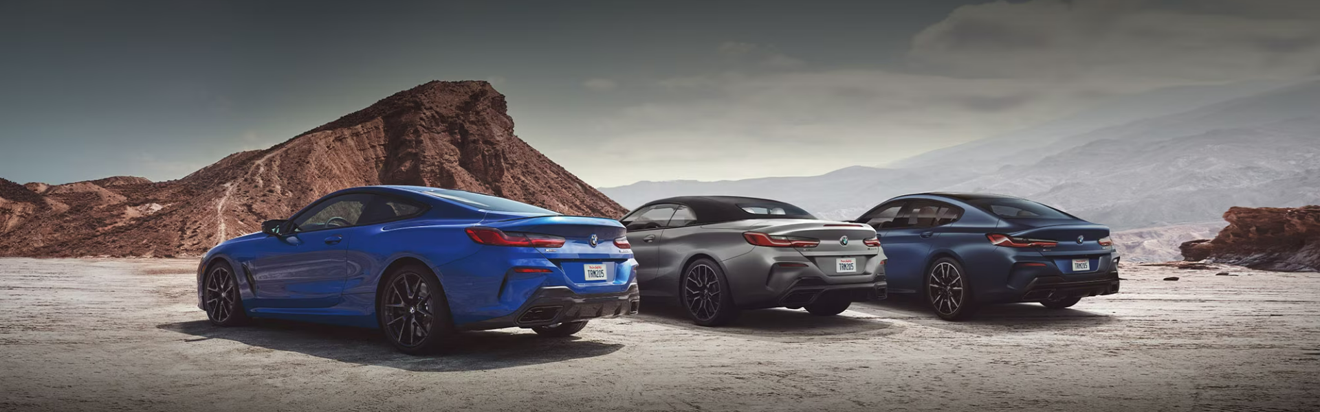 2025 BMW M8 parked in a desert-like landscape with mountains in the background-Banner
