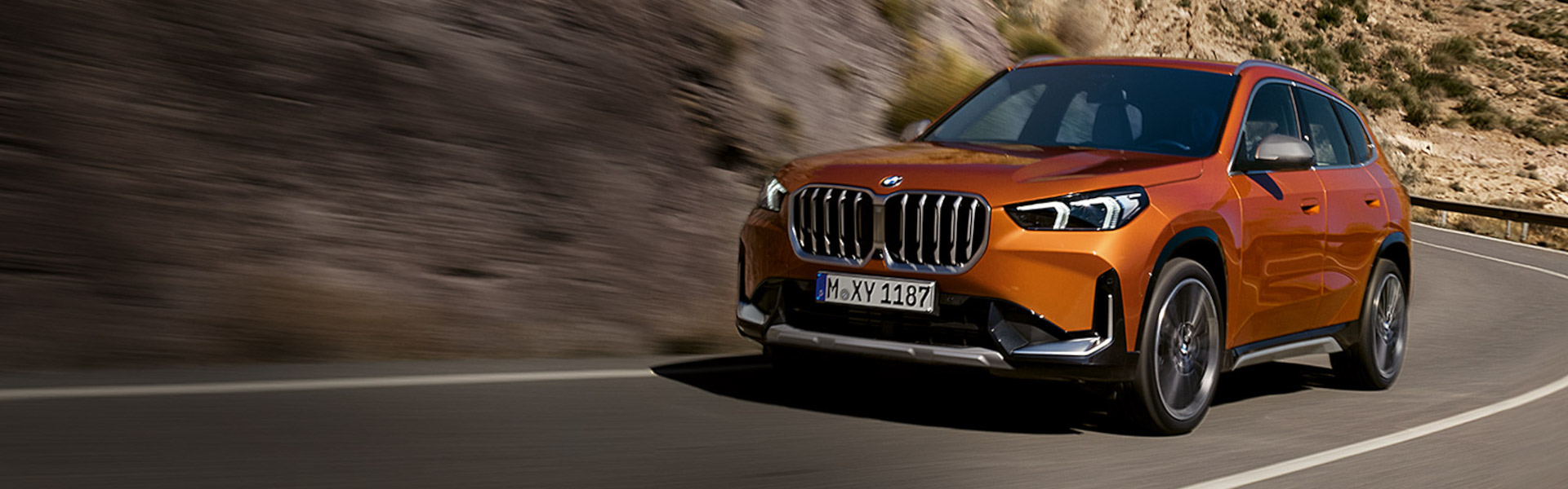 2025 BMW X1 driving along a winding road through a rocky and mountainous area-Banner