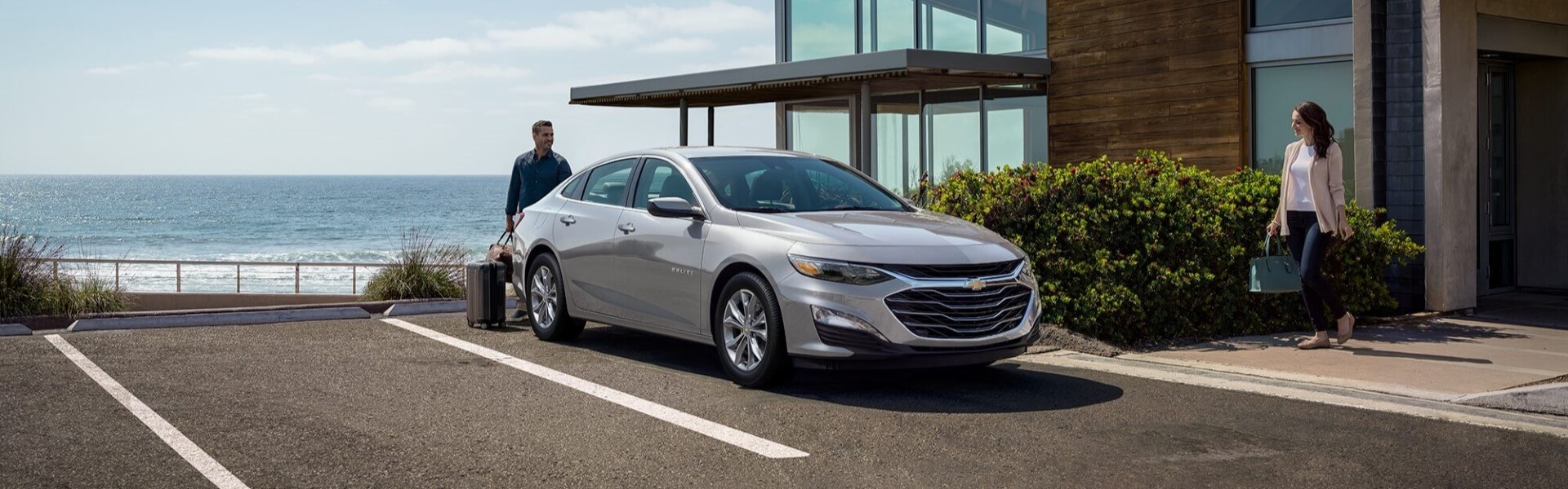 2025 Chevrolet Malibu In Sterling Grey Parked In Front Of A Home Under A Clear Blue Sky For Sale