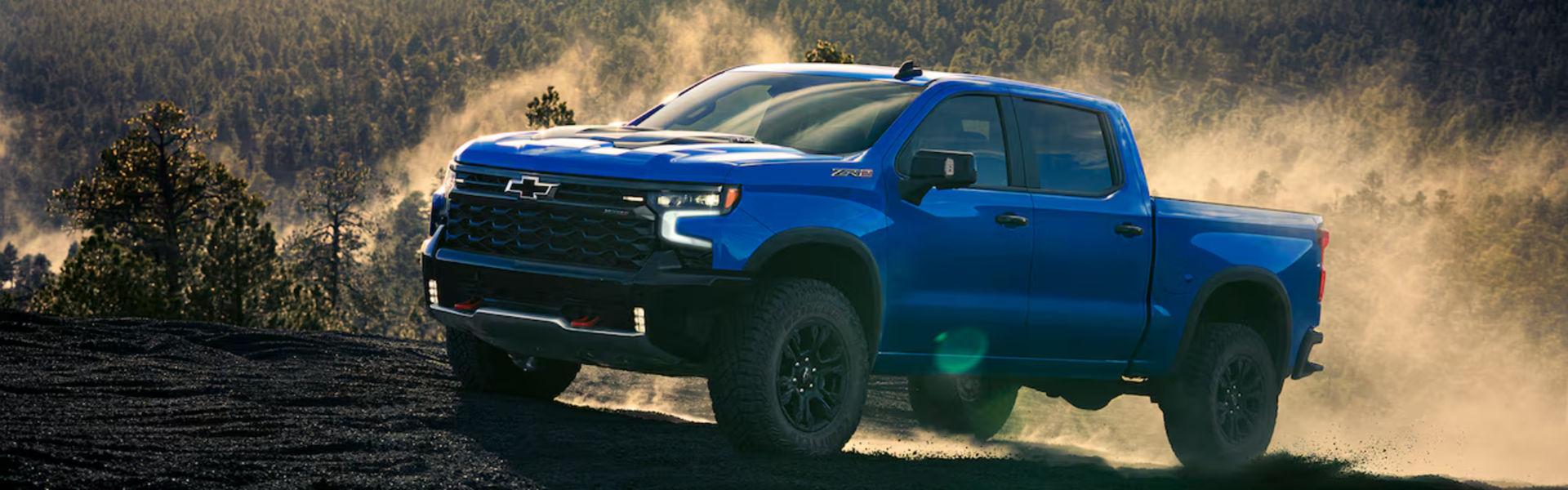2025 Chevrolet Silverado 1500 driving through a rugged, off-road environment with a forested backdrop-Banner