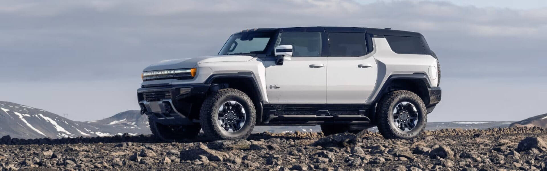 2025 GMC Hummer EV SUV In White Side View On A Rocky Plain Under A Beautiful Blue Sky For Sale