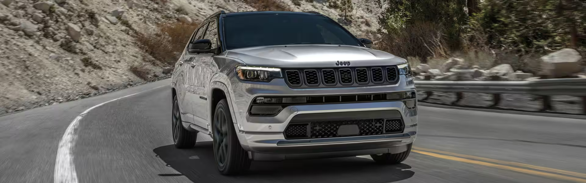 2025 Jeep Compass driving on a winding road with rocky terrain on the side-For Sale