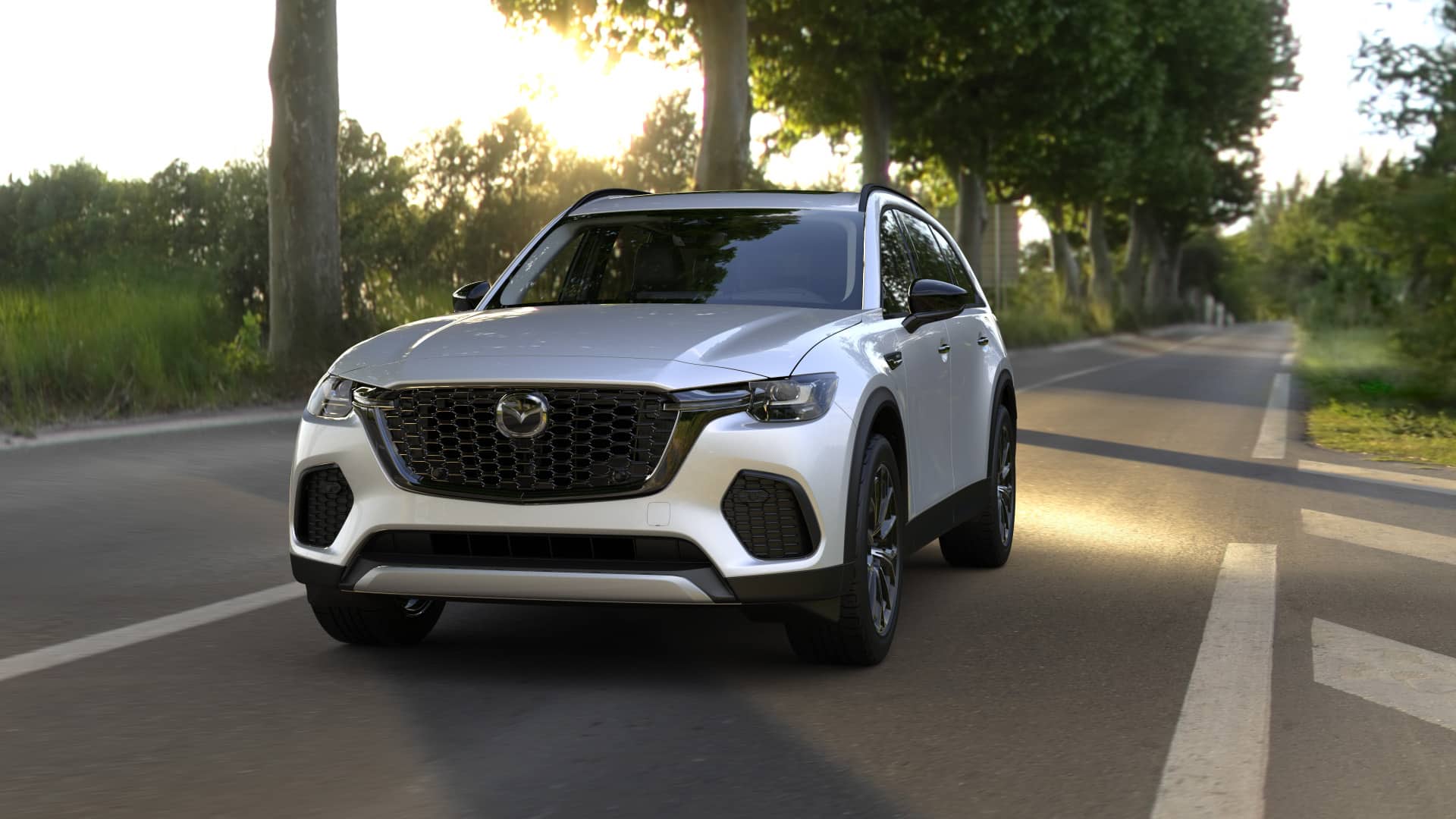 Mazda CX-70 Premium driving through a light wooded road in the evening