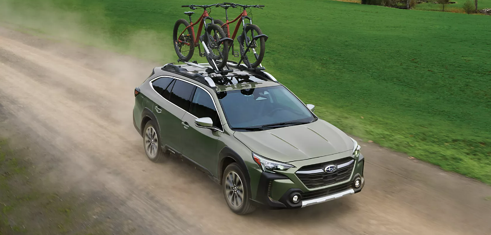 2025 Subaru Outback driving on a dirt road with two bicycles mounted on the roof rack