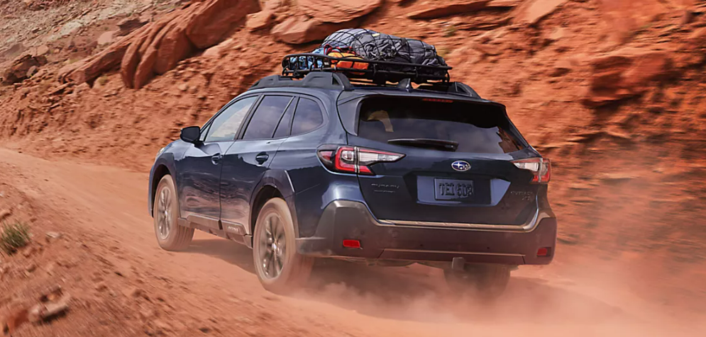 2025 Subaru Outback driving on a dusty, rugged dirt road in a desert or canyon setting