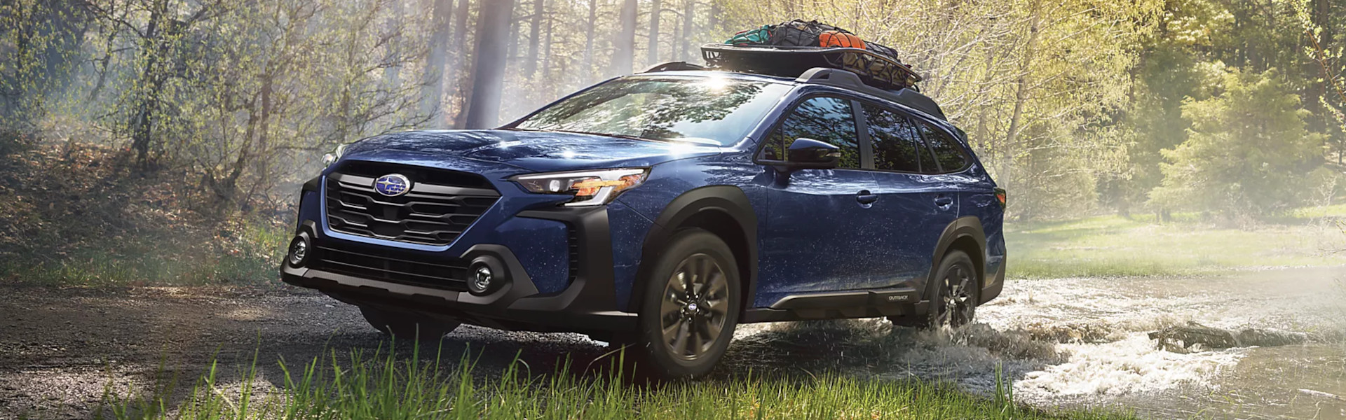 2025 Subaru Outback driving through a shallow stream in a wooded area-Banner