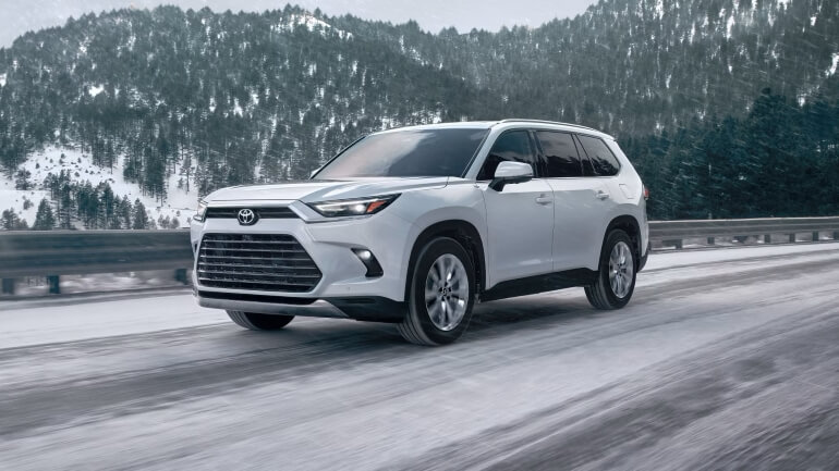 2025 Toyota Grand Highlander Platinum AWD In Wind Chill Pearl Driving On A Snowy Road - Feature Image