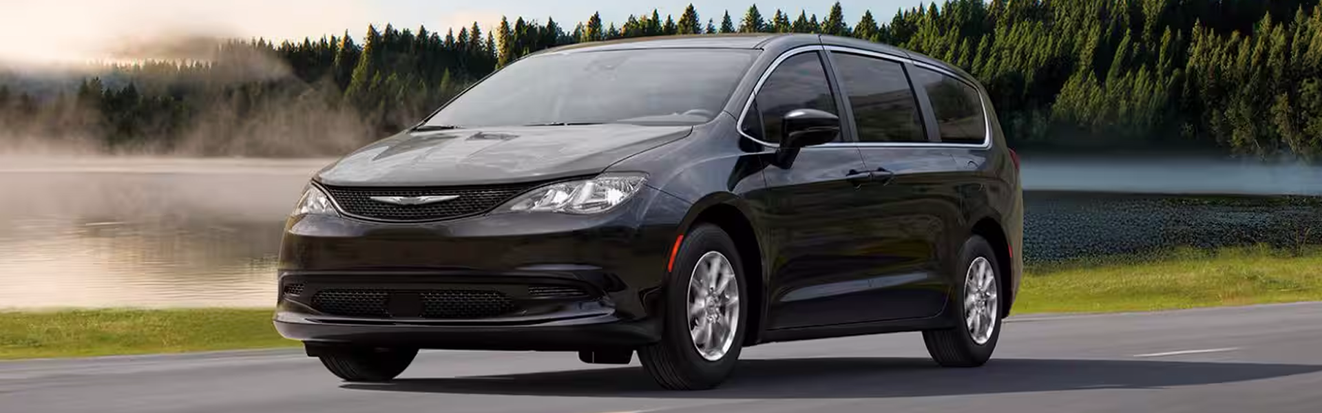 2026 Chrysler Voyager for Sale - Banner - A driver-side front angle of a black 2026 Chrysler Voyager LX traveling on a lakeside highway