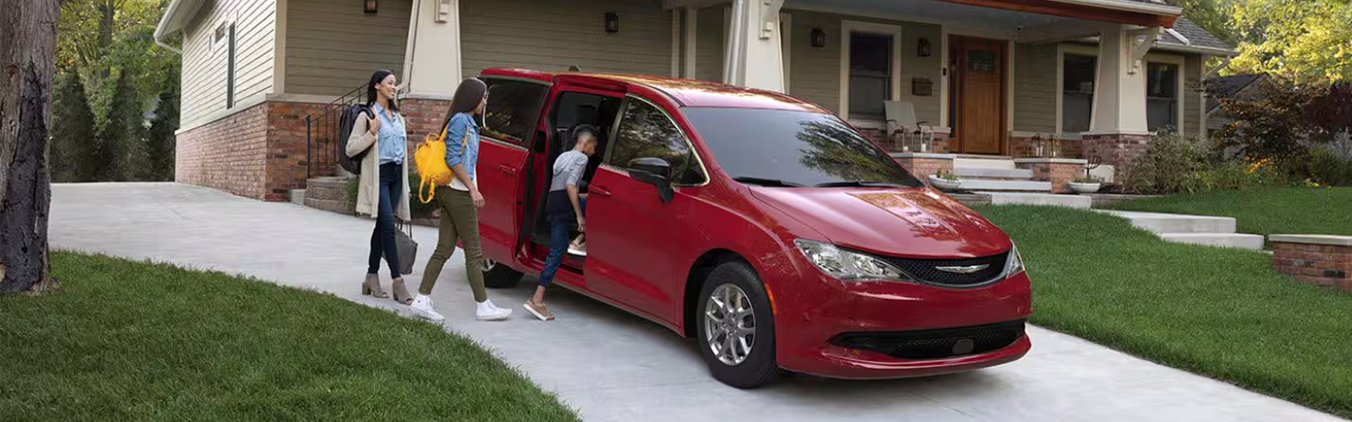 2026 Chrysler Voyager for Sale - Banner - A red 2026 Chrysler Voyager LX parked in the driveway of a home with its passenger-side sliding door open and one of two children entering the vehicle, along with a woman.