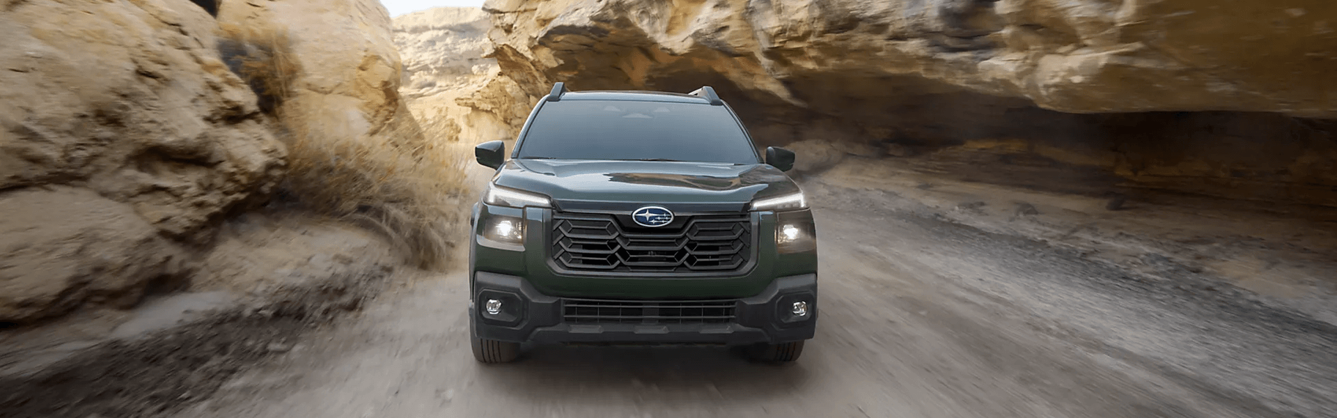 2026 Subaru Outback Driving Straight At the Photographer Between Some Large Desert Rocks Banner