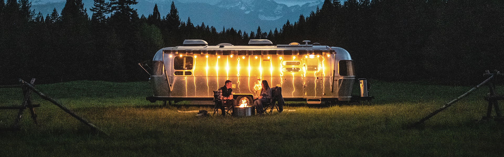 Airstream Globetrotter banner - a couple near a fire pit outside their Airstream