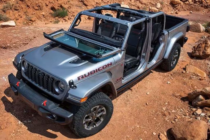 New Jeep Gladiator with 4WD, windshield folded down and doors and roof removed, parked off-road in a clearing.